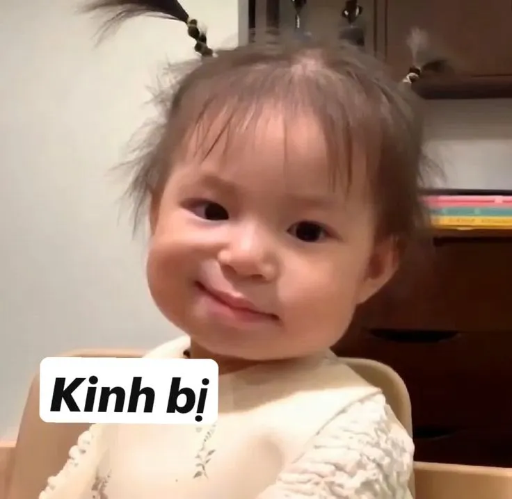17 Em bé mặc váy trắng chỉ tay về phía trước cạnh chữ Kinh bỉ, nụ cười hiền làm pha phán xét trông rất đáng yêu
