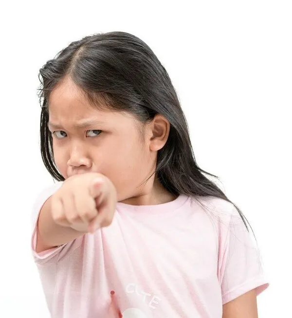6 Cô bé áo hồng đứng nền trắng chỉ tay vào người xem, gương mặt cau có như đang bắt lỗi ai vừa nói sai