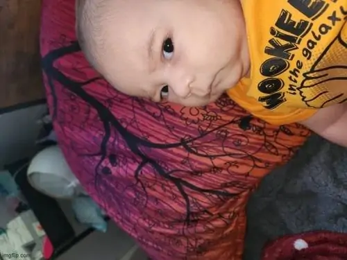 12 Hình chế hài em bé sơ sinh mặc áo vàng nằm trên gối đỏ đang liếc ngang một cách đầy hoài nghi và già dặn trước ống kính máy ảnh.