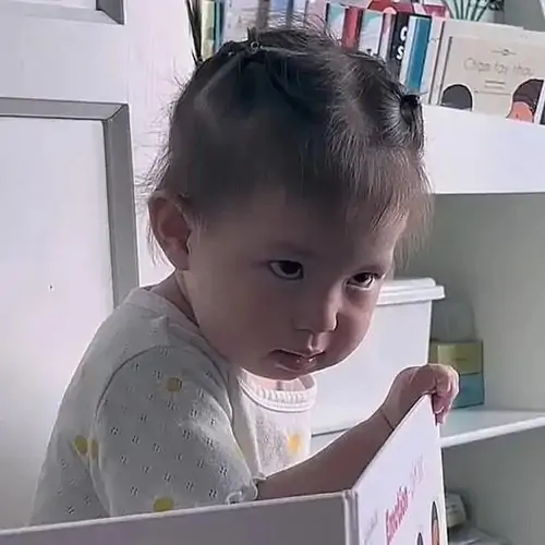 18 Em bé mặc đồ trắng ngoảnh mặt lại lườm một cái sắc lẹm khi đang cầm cuốn sách trên tay tạo nên biểu cảm cụ non cực nhây.
