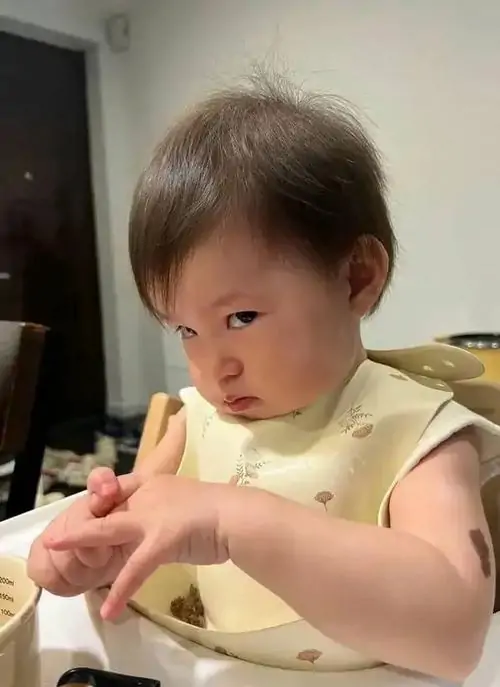 9 Bé gái đeo chiếc yếm ăn màu hồng đang cụp mắt nhìn nghiêng đầy hờn dỗi như đang lên kế hoạch troll bố mẹ vô cùng đáng yêu.