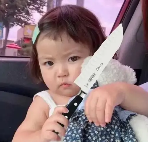 11 Bé gái mặc váy chấm bi nhìn thẳng ống kính, tay cầm vật giống dao trắng tạo vẻ nghiêm túc rất buồn cười