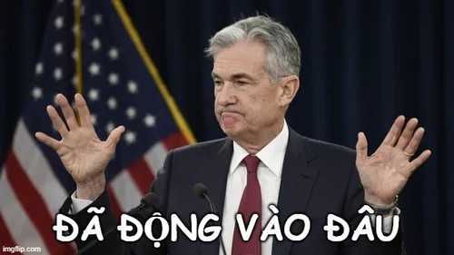 14 Người đàn ông tóc bạc mặc áo vét trước phông cờ, hai tay giơ lên như đang phủ nhận chuyện vừa bị nhắc