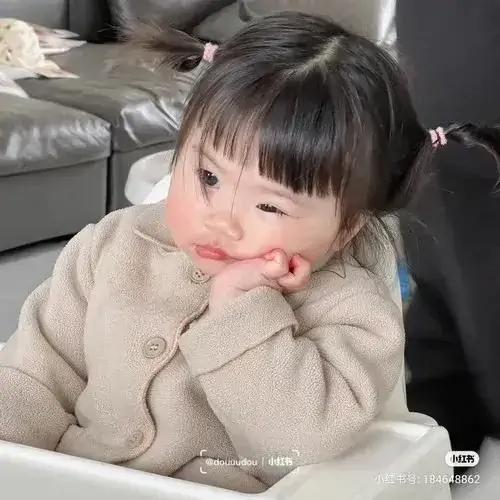 13 Hai bàn tay áp lên má, bé mặc áo bông màu kem chu môi nhìn ra ngoài như đang chờ được dỗ dành