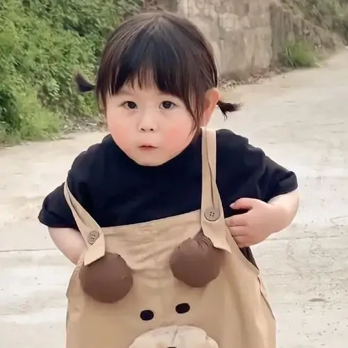 20 Hình ảnh bé yêu đứng ngoài trời trong yếm gấu nâu, mắt nhìn thẳng nghiêm túc như đang kiểm tra ai vừa gọi tên mình