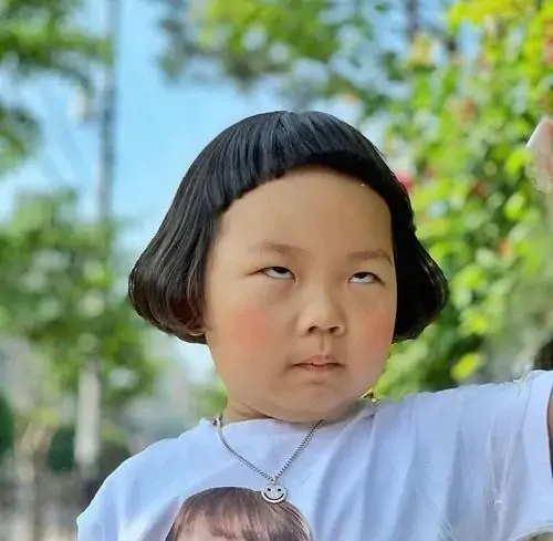 25 Cô bé tóc ngắn mặc áo trắng nhìn nghiêng với ánh mắt khó hiểu, biểu cảm như đang nghe một câu chuyện hơi sai