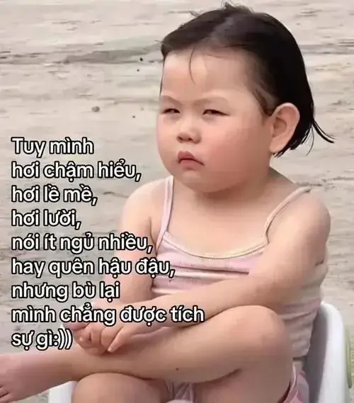5 Bé nhỏ áo trắng ngồi khoanh chân bên bãi cát, ánh mắt nghiêm nghị cùng dòng chữ dài tạo cảm giác cà khịa rất khẽ