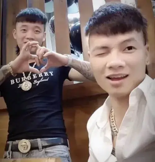 19 Hai chàng trai trong phòng tự chụp trước gương, một người áo đen ôm tay thành tim còn người áo trắng cười hơi ngượng