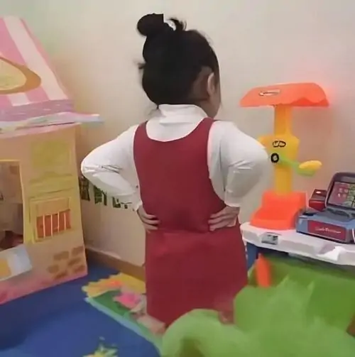 22 Em bé mặc chiếc váy đỏ yếm đứng quay lưng lại ống kính với đôi tay nhỏ xíu chống vào hông ra dáng giận dỗi giống ảnh meme chống nạnh.