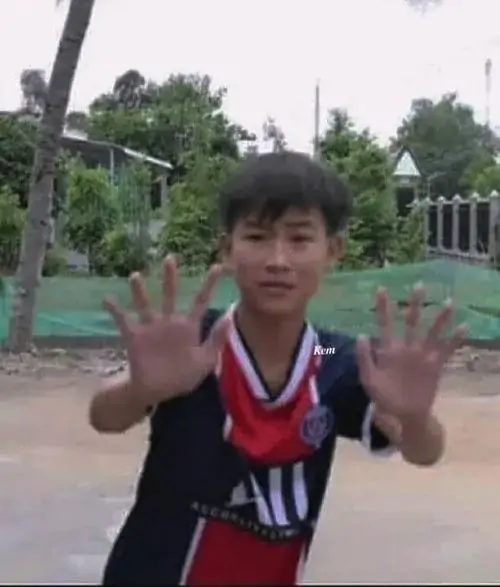 19 Cậu bé mặc áo thể thao đỏ đen đứng ngoài sân, hai tay xòe rộng như chấm 10 cho chính pha tạo dáng của mình