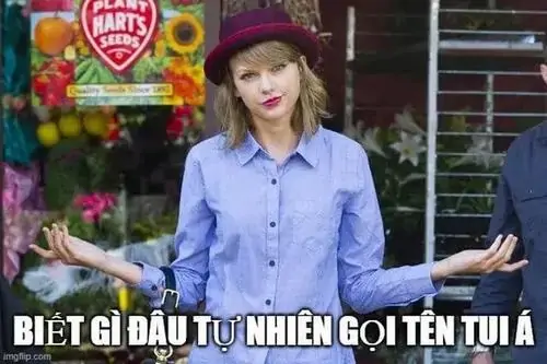 5 Cô gái áo xanh đội mũ tím đứng trước quầy đồ chơi, dang tay phân bua với dòng chữ tự nhiên gọi tên tui à