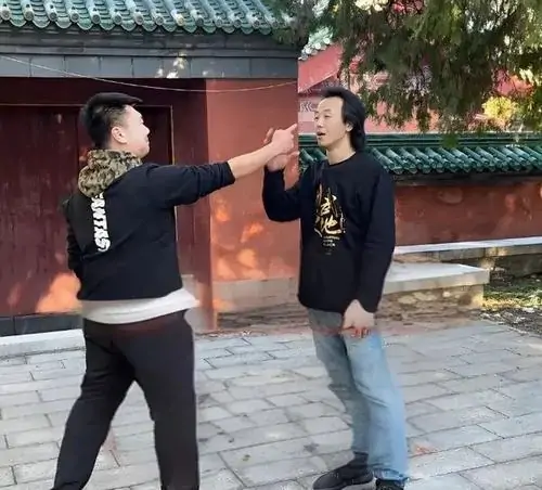 2 Hai người đàn ông mặc áo đen đứng ngoài sân, một người chỉ tay sát mặt người kia như đang bắt lỗi rất nghiêm túc.