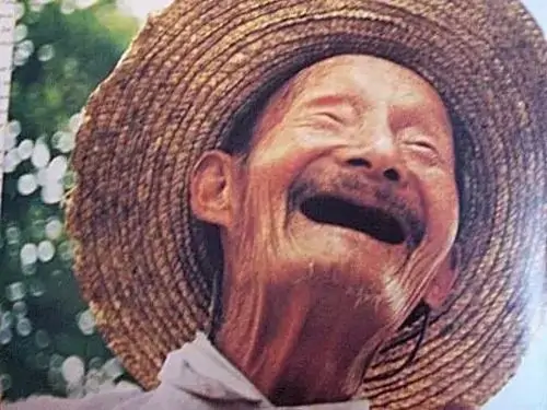 13 Ông lão đội nón rơm cười lớn giữa nền hoa lá, khuôn mặt nhăn nheo lại càng làm nét vui thêm chất đời