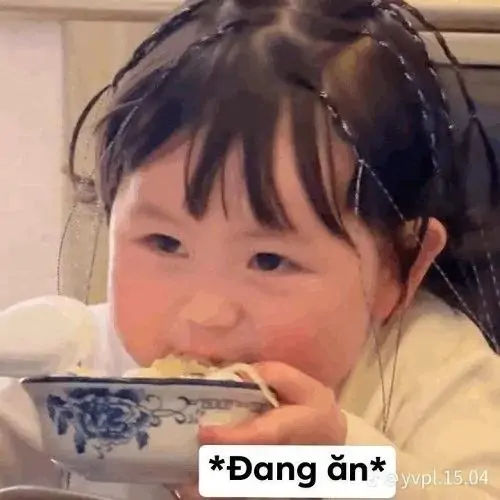 33 Bé gái đang ăn trong bát lớn, tóc kẹp gọn hai bên, dòng chữ đang ăn làm mặt ngơ thêm dễ thương
